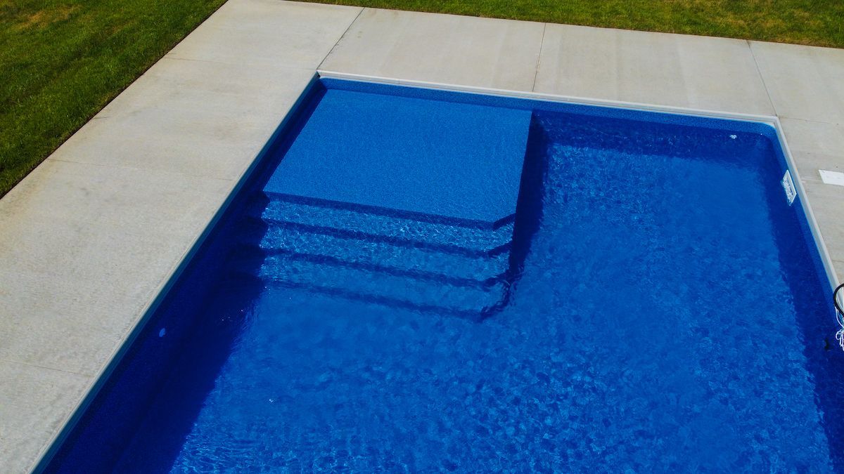 Blue swimming pool with steps and light-colored deck surrounding it