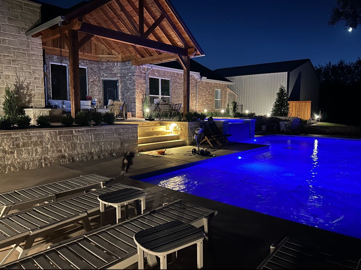 A large swimming pool is lit up at night in front of a house.