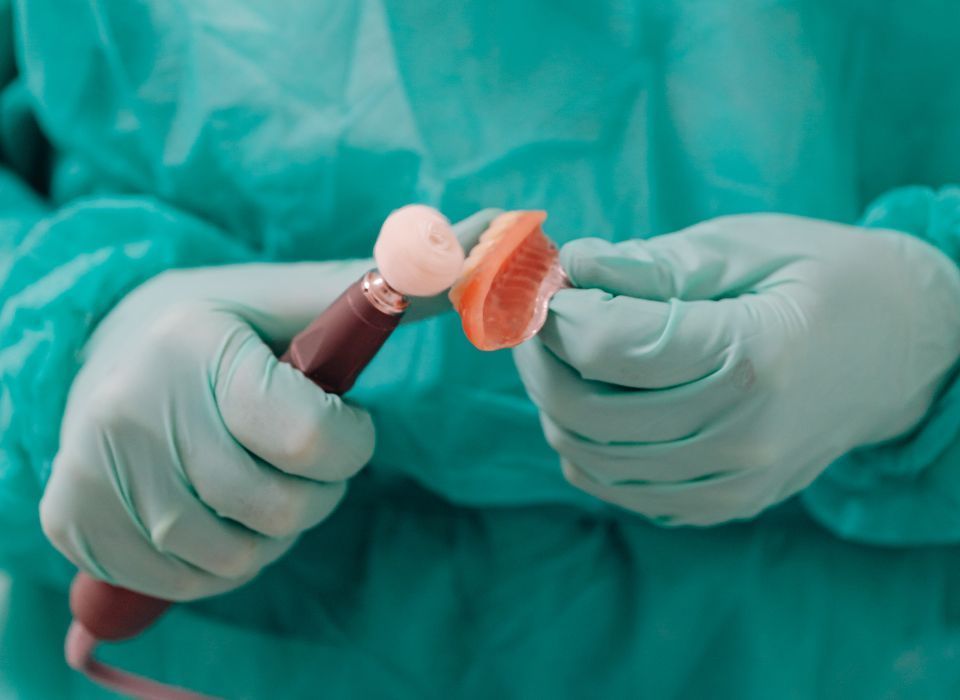 Gloved hands holding dental appliance, polishing tool. Green surgical attire visible.
