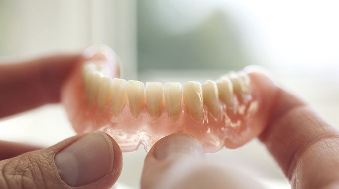 Person holding a set of upper dentures, with pink base and white teeth.