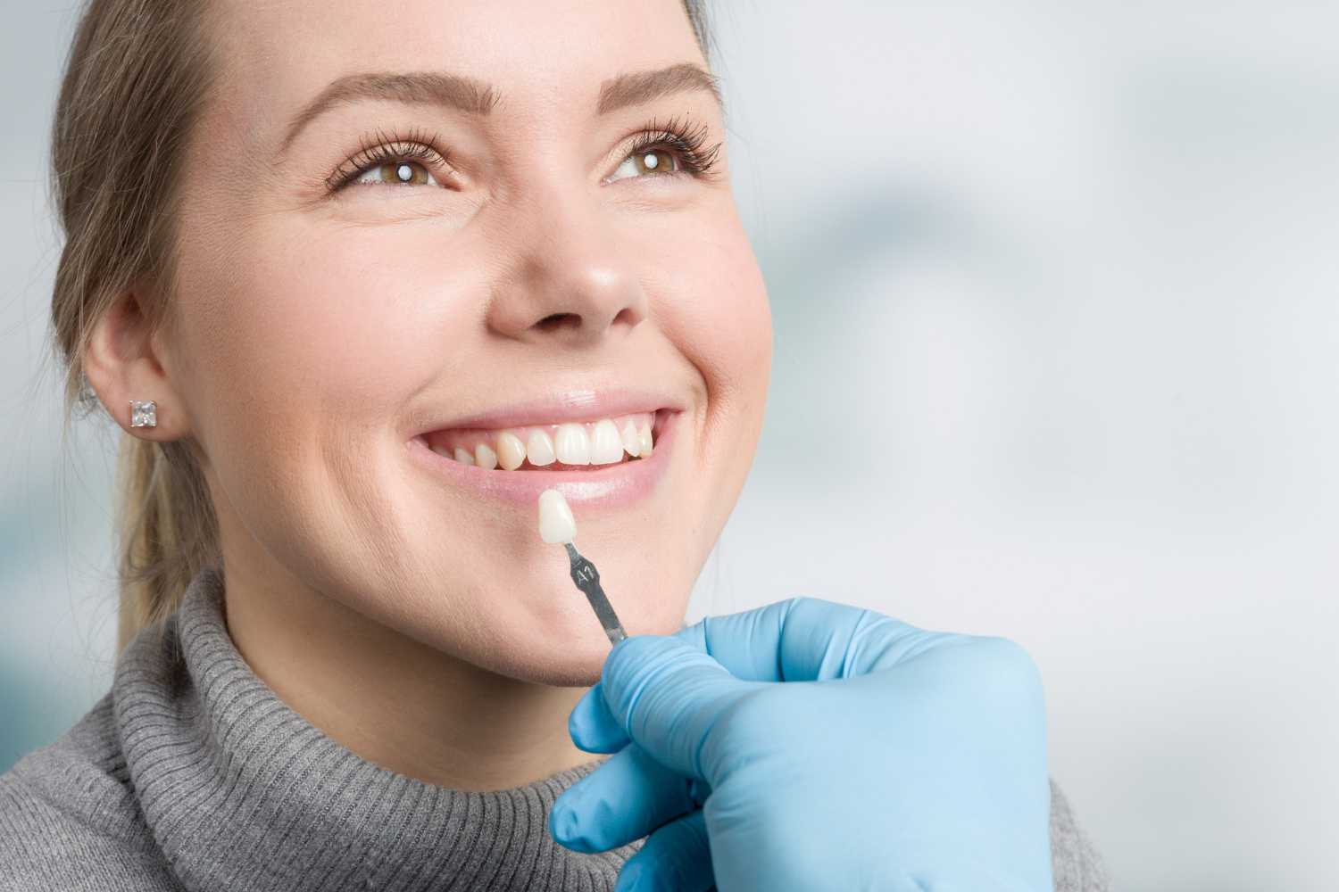 Woman smiling while a dentist holds a tooth shade guide to her teeth.