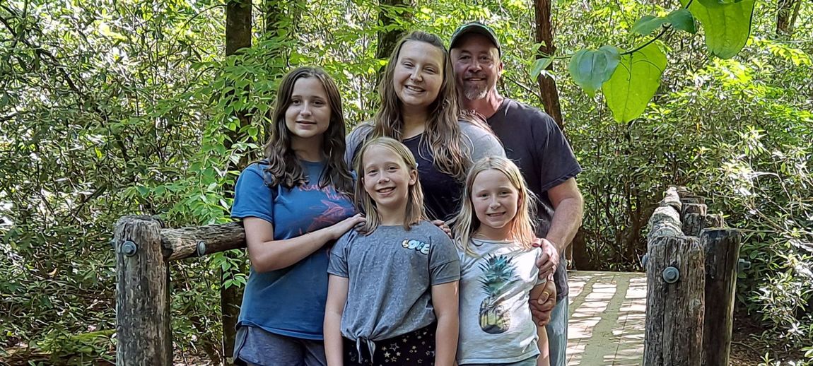 A family is posing for a picture on a bridge in the woods.