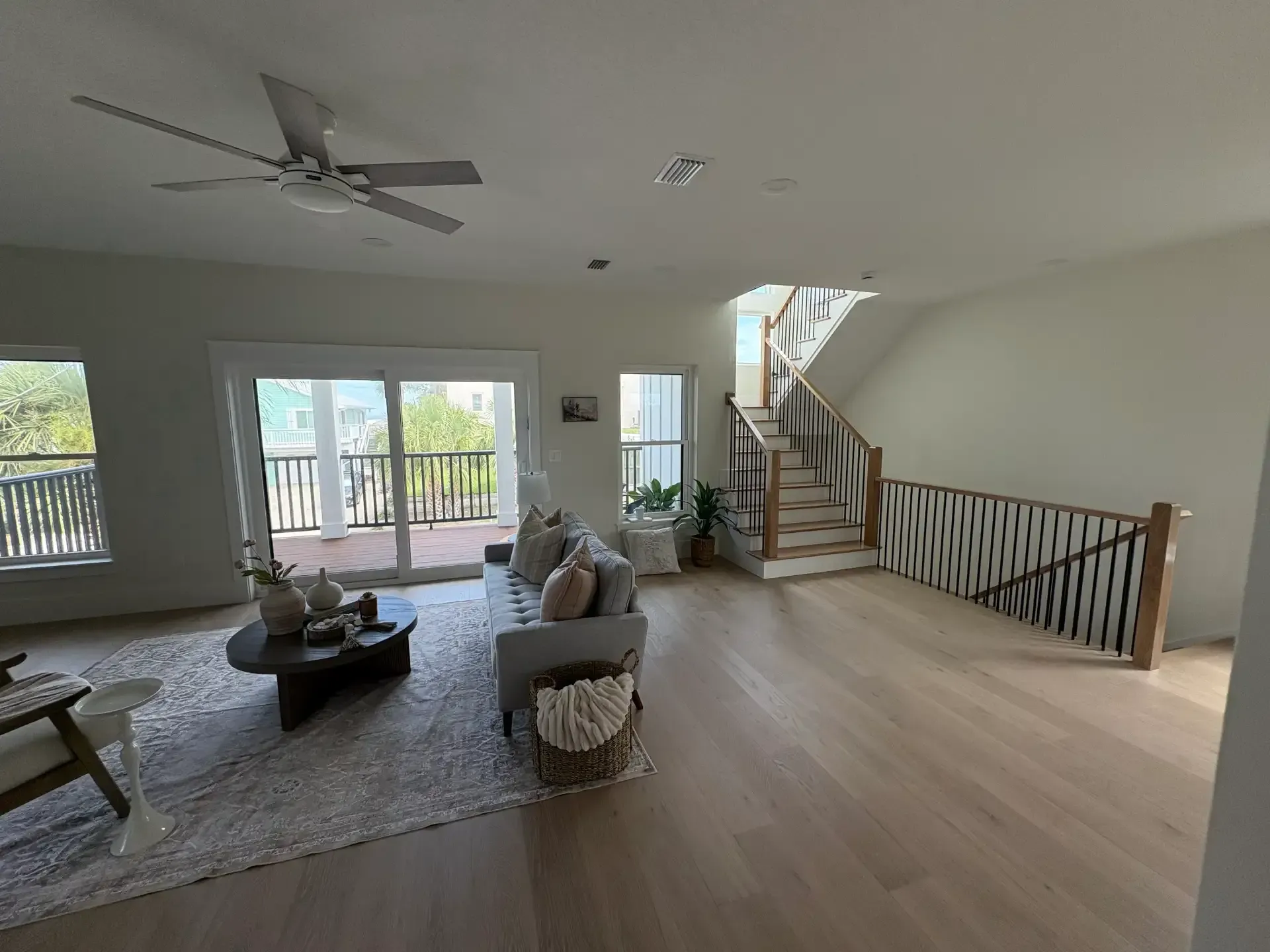 Spacious living room with vaulted ceiling, large windows, staircase, and light wood floors.