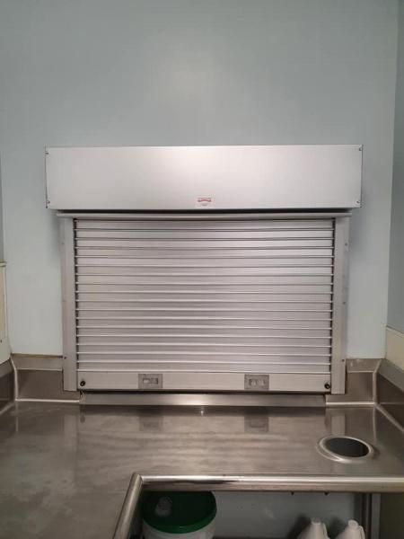 Closed metal service window with a shutter in a tiled interior room.