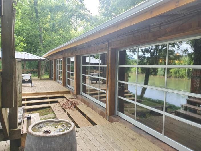 Wooden deck beside a lakeside cabin with large windows, steps, and trees around it