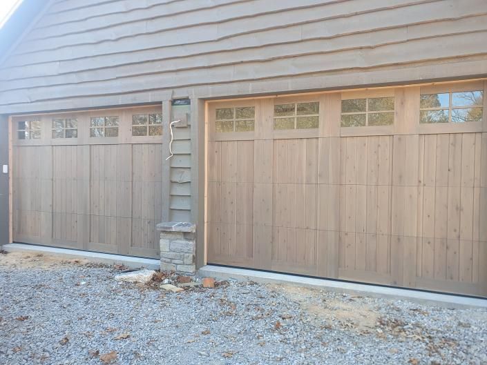 Two light wood garage doors with frosted windows on a beige house exterior