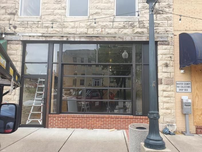 Storefront with large black-framed windows, brick base, ladder on the left, and a streetlamp in front.