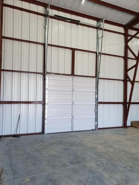 Empty metal warehouse interior with white paneled doors and concrete floor
