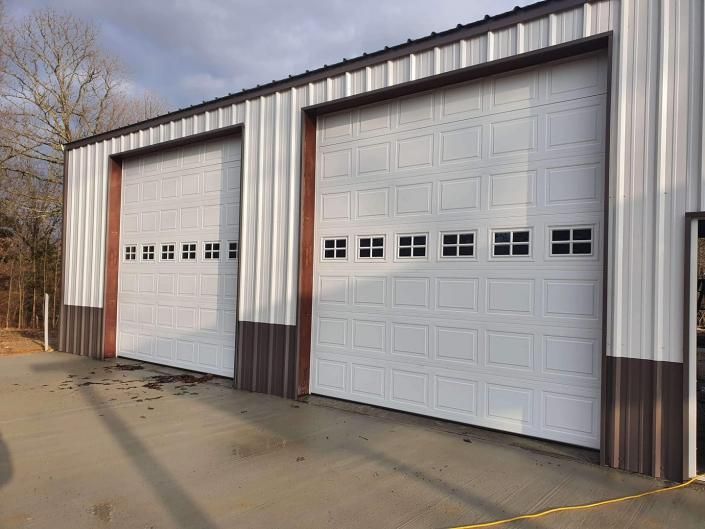 Two white garage doors on a metal-sided building beside a concrete lot