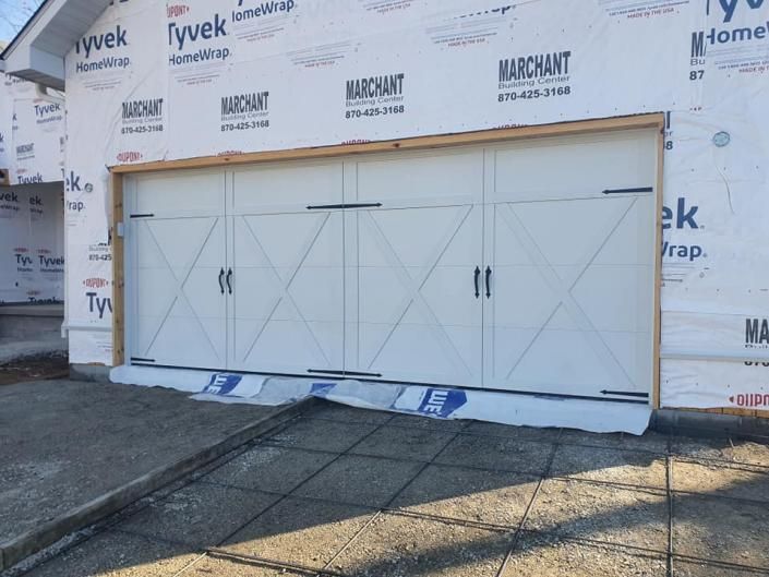 White garage door on a building under construction, with Tyvek house wrap and blue protective coverings on the ground