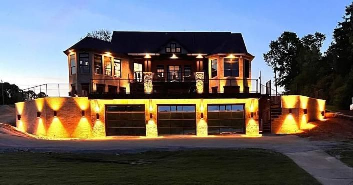 Illuminated two-story brick house with lit garage doors at dusk