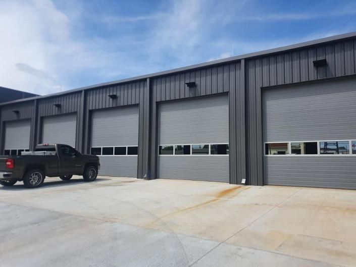 Industrial building with three gray garage doors and a black pickup truck in front