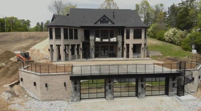 Large unfinished house under construction with stone terrace and glass lower level in a wooded setting