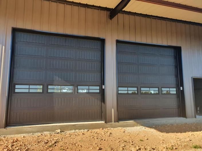 Two dark brown garage doors on a beige industrial building with a dirt foreground