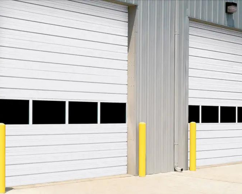 Industrial building with two white garage doors and yellow safety bollards
