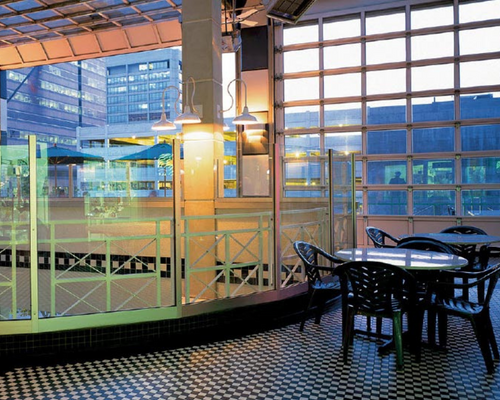 Empty indoor café seating by large windows at dusk, with a checkered floor and modern glass walls
