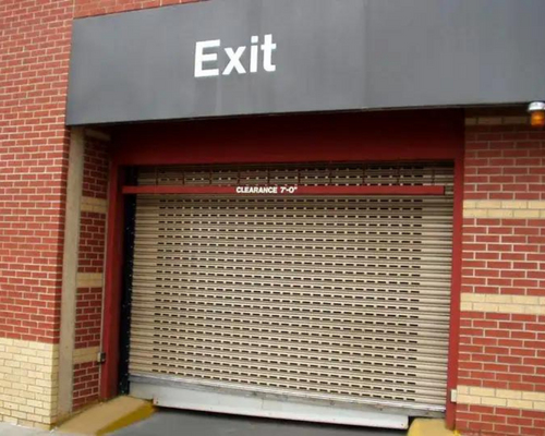 Closed metal exit gate under a gray “Exit” sign on a brick building.