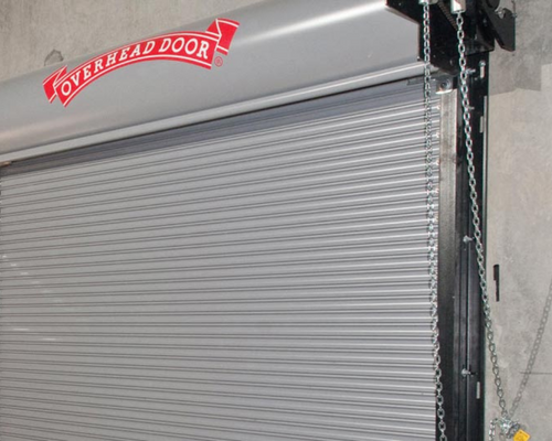 Closed gray roll-up garage door with red “Overhead Door” sign