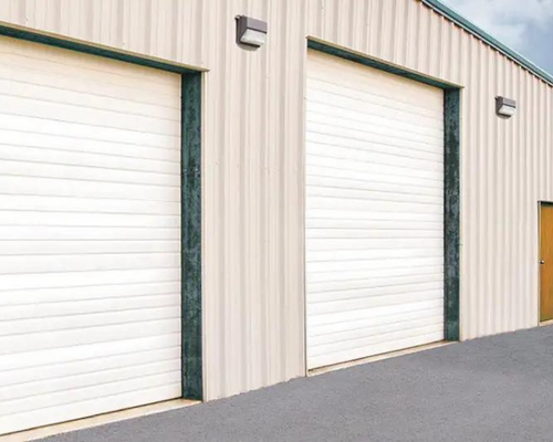 Two white roll-up garage doors on a beige metal industrial building