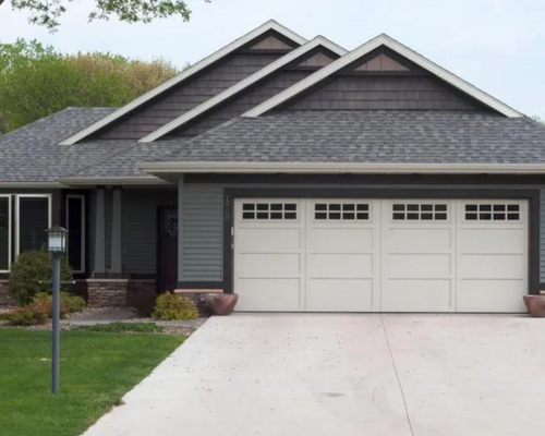 Suburban house with gray roof, white garage doors, and a concrete driveway