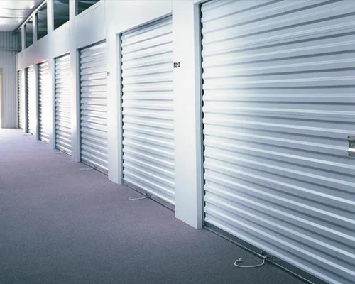 Row of closed silver storage unit doors along a hallway with gray carpet