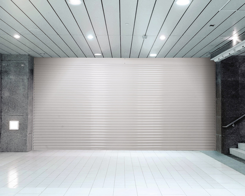 Empty modern lobby with white tiled floor, metallic ceiling lights, and a large closed gray shutter wall