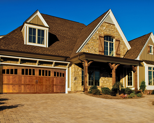 Large brick suburban house with a wooden garage door and gabled roof in warm sunlight