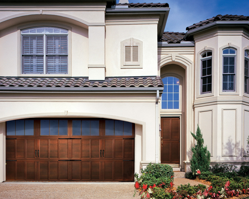 Modern two-story house exterior with a brown garage door, arched windows, and landscaped front entrance