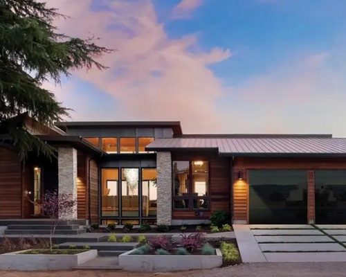 Modern brick house exterior at dusk with warm interior lights, garage, and landscaped front yard
