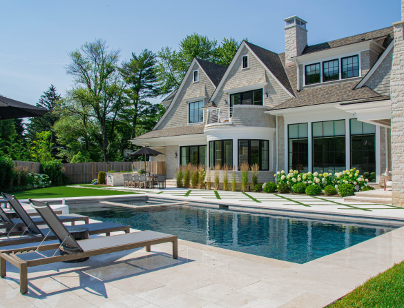 Luxury home backyard with swimming pool, lounge chairs, and stone patio under clear blue sky