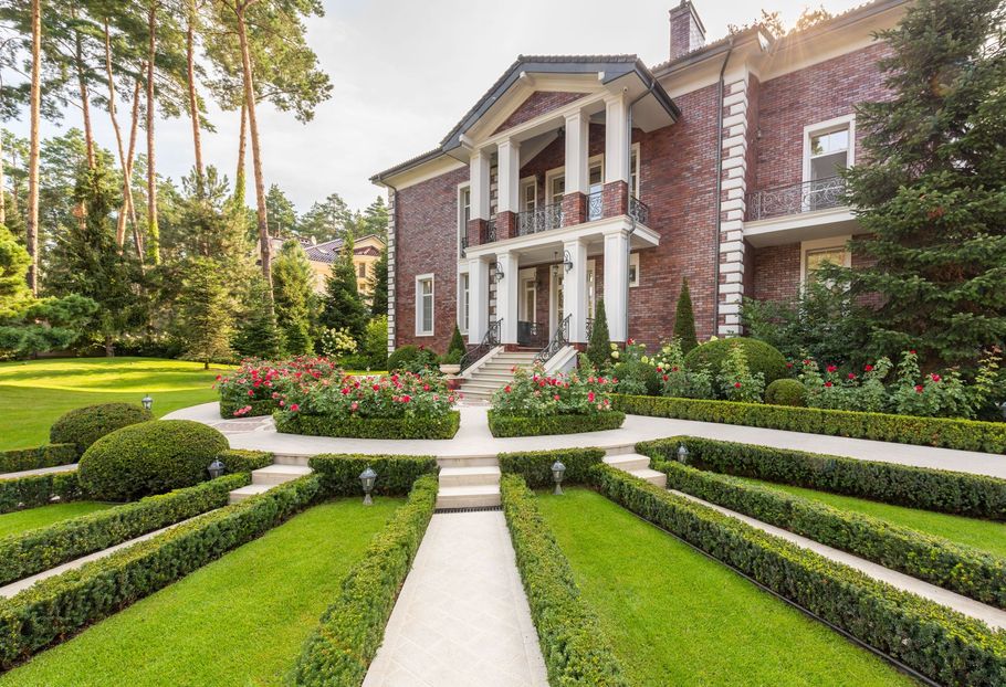 Brick mansion with white columns, formal garden hedges, and a central stone walkway