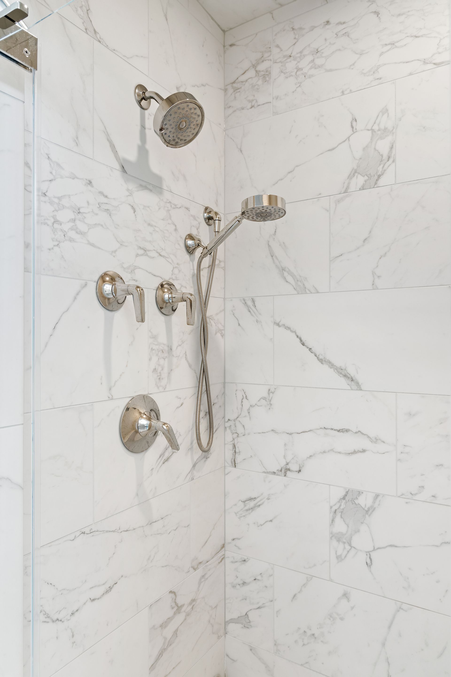 Marble tile shower with chrome fixtures, handheld sprayer, and dual control handles
