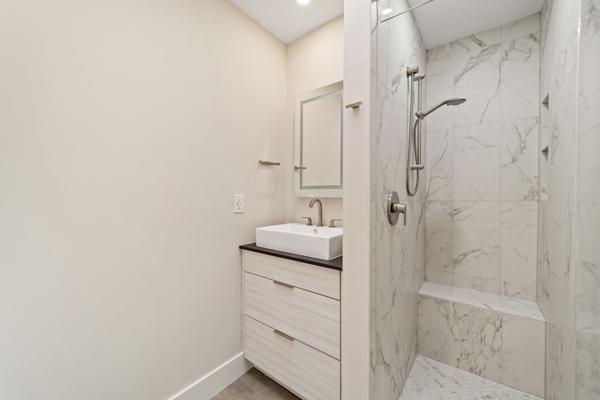 Modern bathroom remodel in Washington DC with marble tile shower, vessel sink, light wood vanity, and brushed nickel fixtures