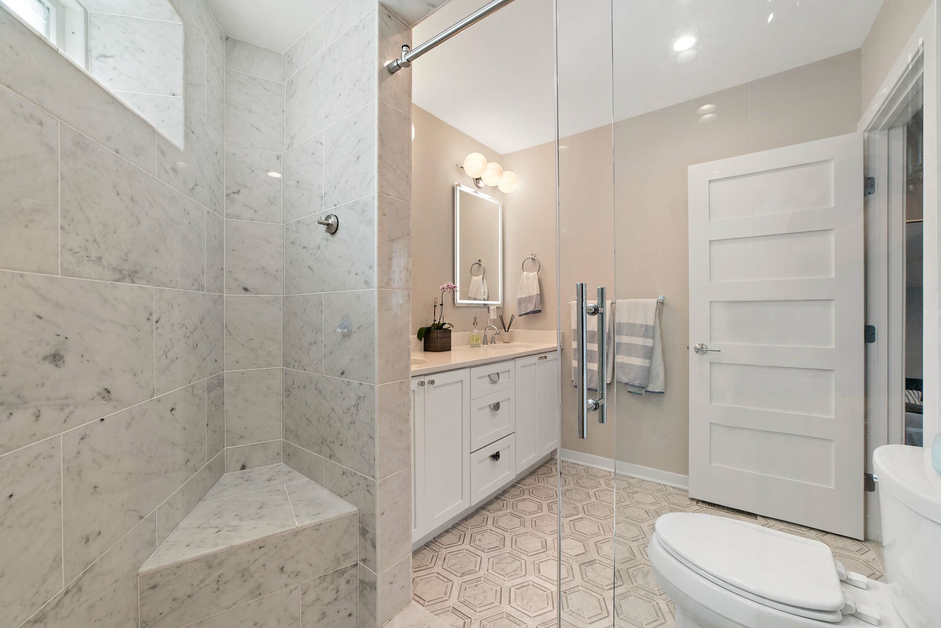 guest bathroom remodel with marble tile shower bench and white double vanity with LED mirrors