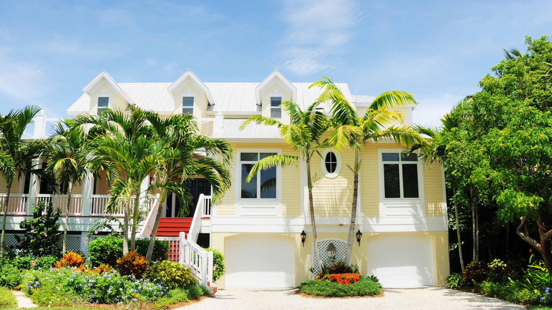 Bright white tropical house with palm trees, lush garden, and a garage under a sunny blue sky
