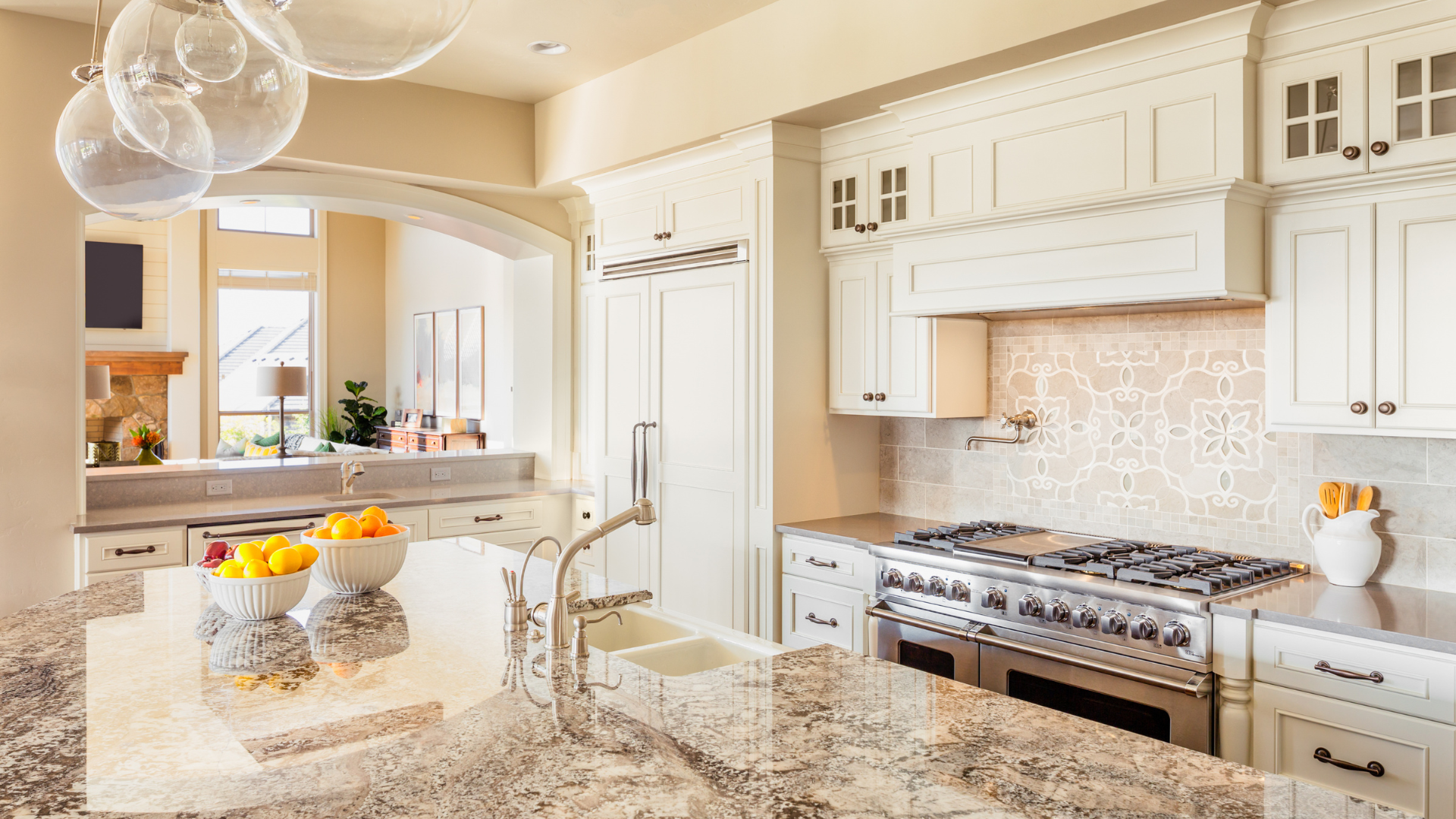 Bright modern kitchen with white cabinets, granite island, and stainless steel stove, lit by pendant lights