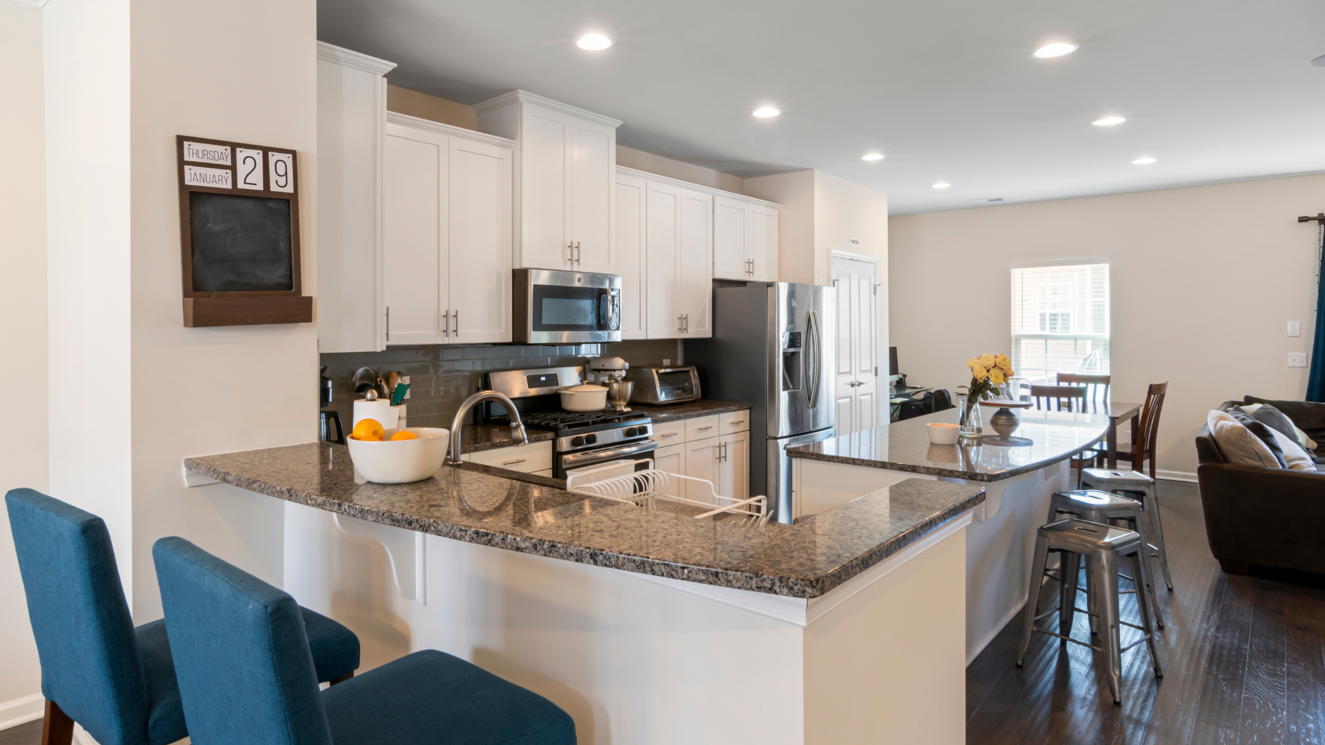 Bright modern kitchen with white cabinets, granite island, and blue chairs in an open dining area