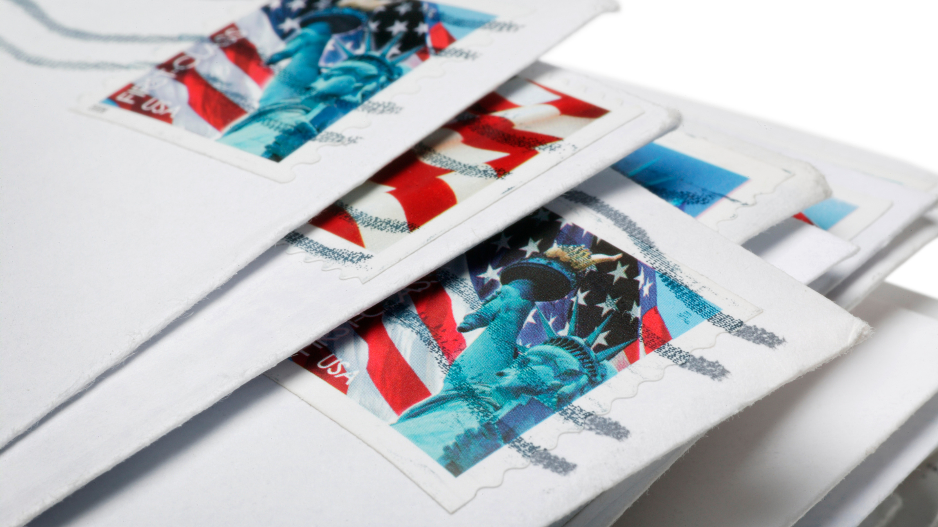 Stacked red, white, and blue envelopes with postage stamps on a white surface