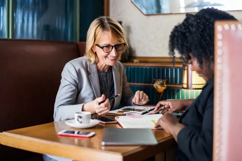 Two women are sitting at a table in a restaurant having a meeting.