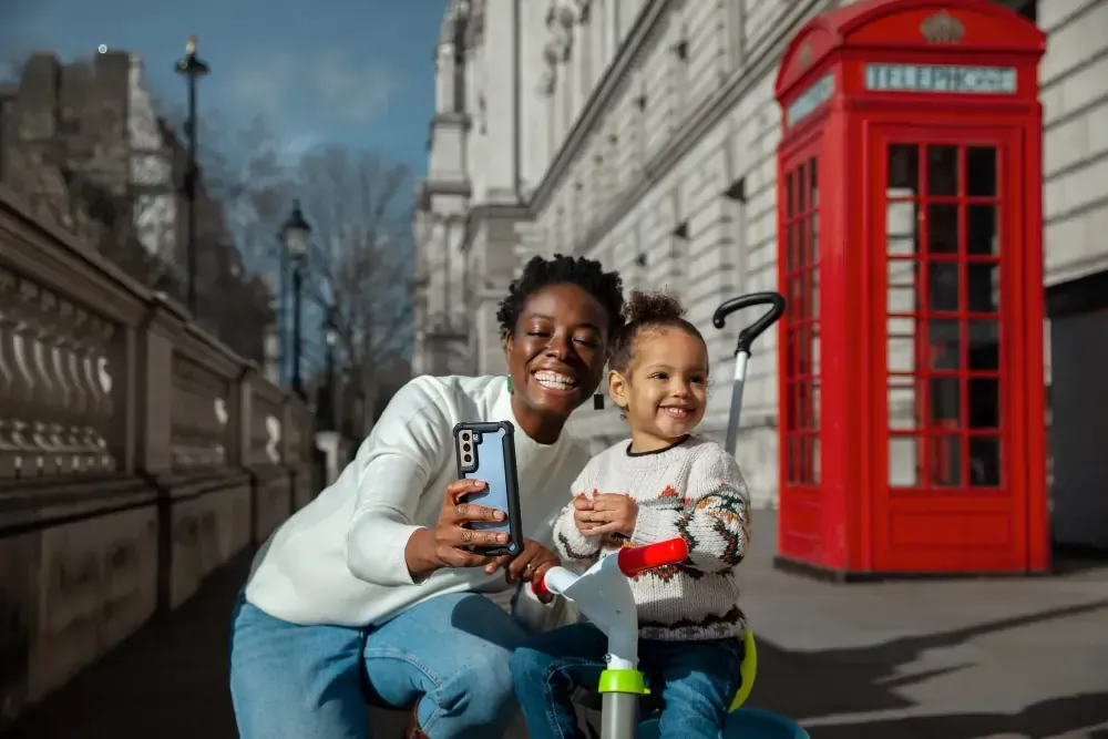 A woman and a child are taking a selfie in front of a red telephone booth.