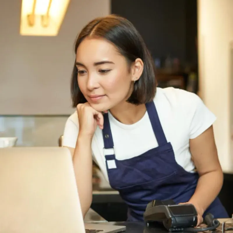 A woman in an apron is looking at a laptop computer