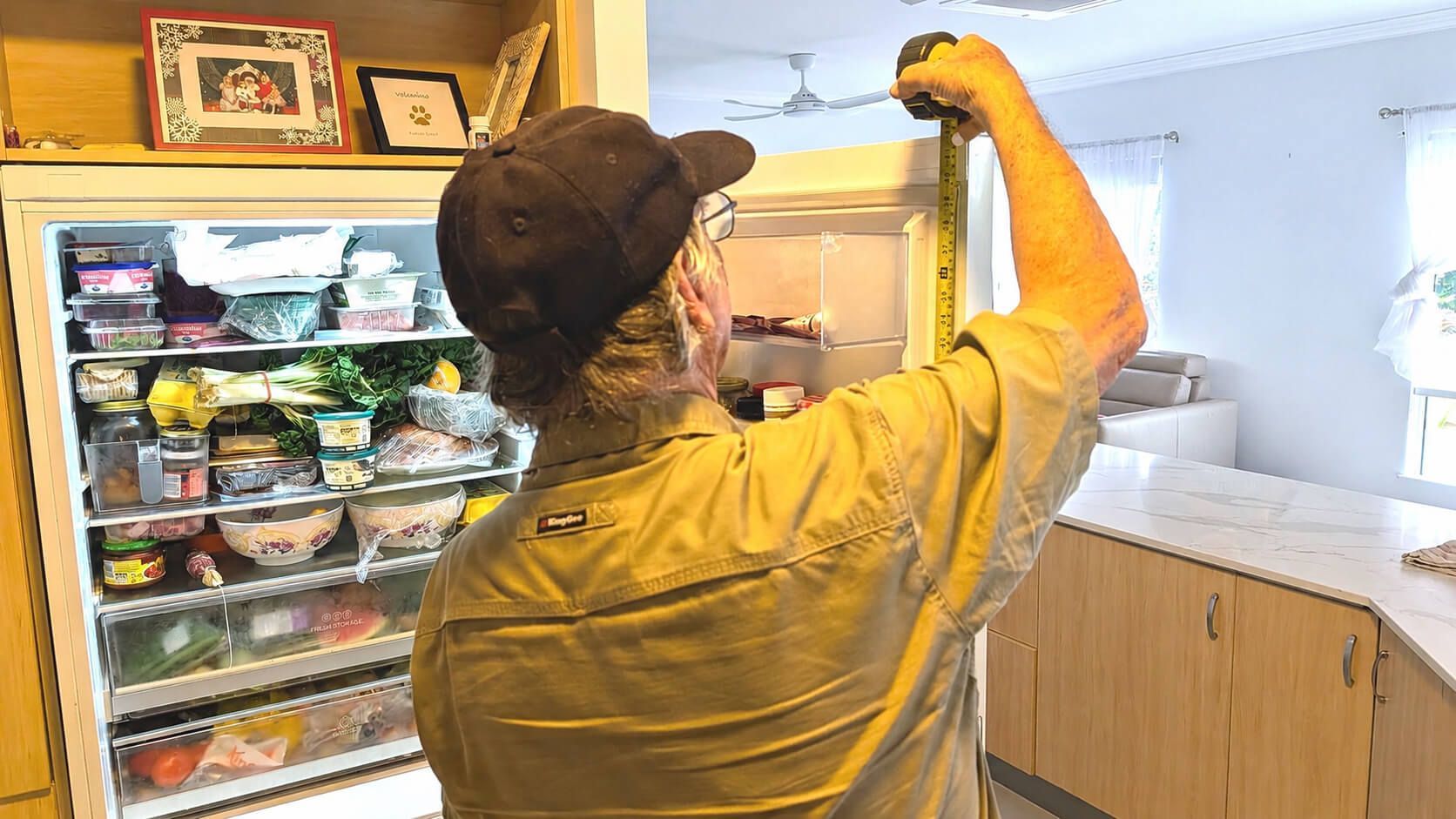 Person Reaching Into an Open Refrigerator in a Bright Kitchen — Ace Fridge Door Seals In Cairns, QLD