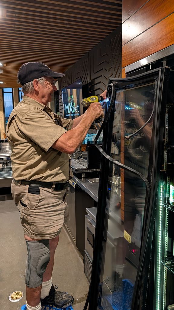 Man Adjusting a Large Glass Panel in a Modern Indoor Space — Ace Fridge Door Seals In Cairns, QLD