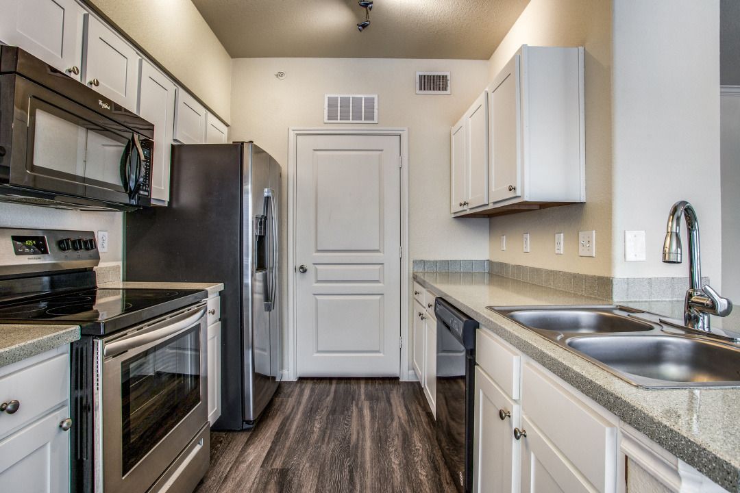Modern apartment kitchen with stainless steel appliances, white cabinets, and a double sink.