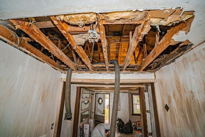 Water-damaged room with a collapsed ceiling exposing wooden beams and hanging debris.