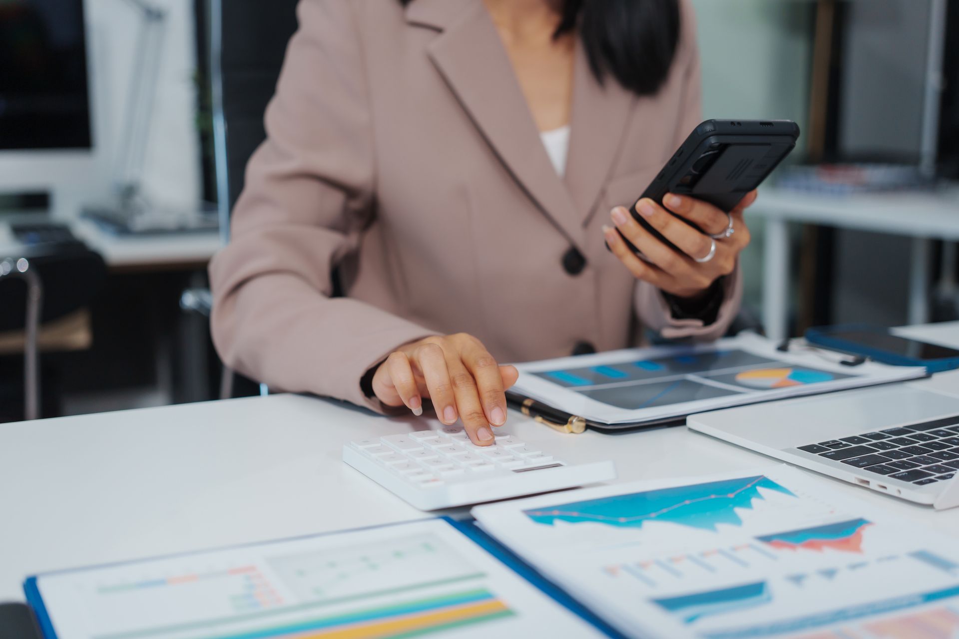 Businesswoman using calculator and phone at desk with charts and laptop. Businesswoman using calculator and phone at desk with charts and laptop.