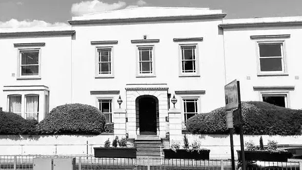 A black and white photo of a large white building with a fence around it.