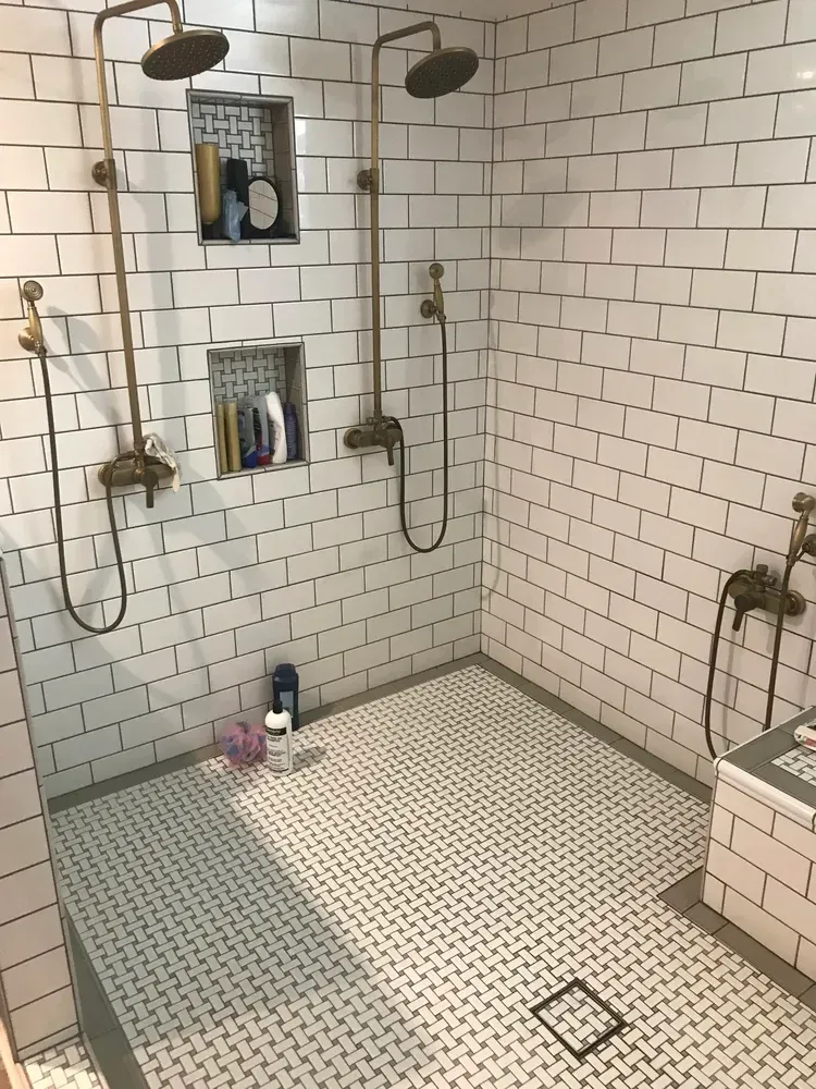 White tiled shower with two shower heads and recessed shelves.