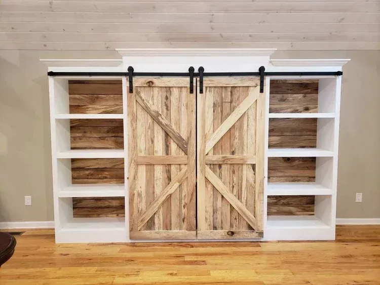 Built-in white bookshelves with sliding barn doors, rustic wood paneling, and black hardware.