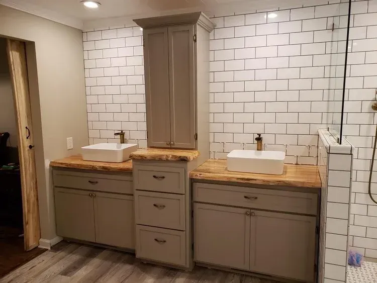 Bathroom with gray cabinets, white sinks, wood countertops, and subway tile.